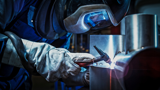 Close-up of male welder wearing helmet while working with welding torch in factory.