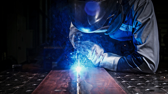 Close-up of male welder wearing helmet while working with welding torch in factory.