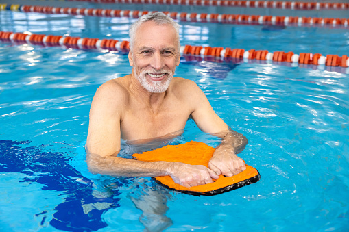 In the swimming pool. Smiling senior gray-haired man swimming