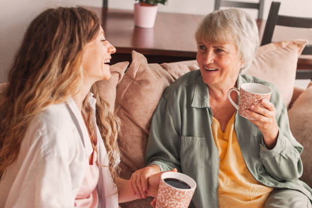 幸せな大人の娘と年配の母親が家のソファに座って話を楽しんでいる - grandmother senior adult smiling women ストックフォトと画像