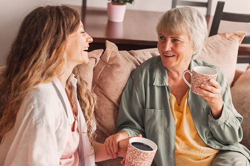 Cheerful old mother and young adult woman talking laughing together, smiling elderly older mum having fun chatting with grown daughter, two age generations pleasant conversation at home concept