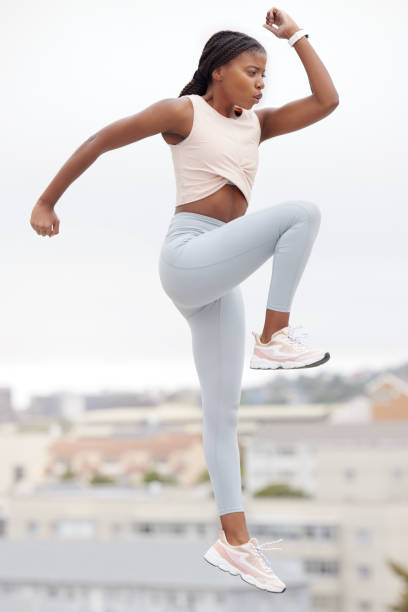 Black woman, jump and fitness while workout, exercise and training in Brazil, city and body warm up for health and wellness. Young female athlete, jumping and cardio practice outdoor in a urban town mujer negra, salto y fitness mientras entrena, hace ejercicio y entrenamiento en brasil, la ciudad y el calentamiento corporal para la salud y el bienestar. joven atleta femenina, salto y práctica cardiovascular al aire libre en una ciudad urbana