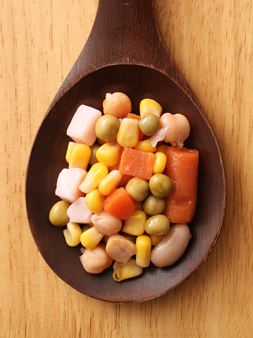 Top view of wooden spoon with boiled vegetables and legumes salad on it