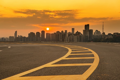 An empty highway during a beautiful sunset against a background of a cityscape with modern buildings