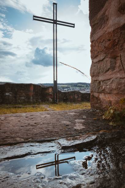 A vertical shot of a cross on Wartenberg castle ruins and its reflection in a puddle