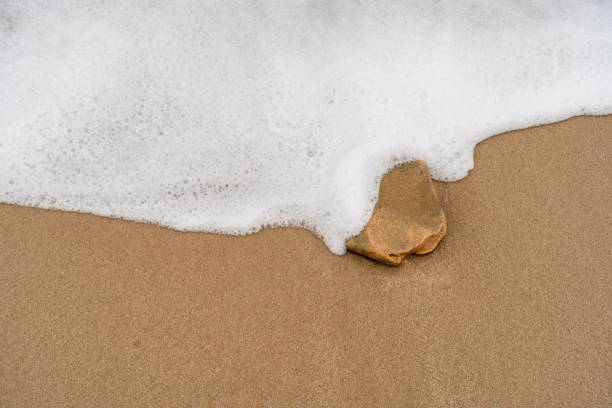 istock View of a wave hitting stone on a sandy beach 1459559768