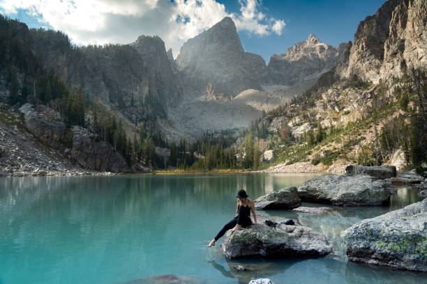 istock Woman sitting alongside a blue lake amidst towering mountains and cliffs 1459560590