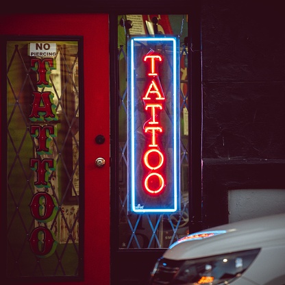 The neon sign of a tattoo shop on the street.