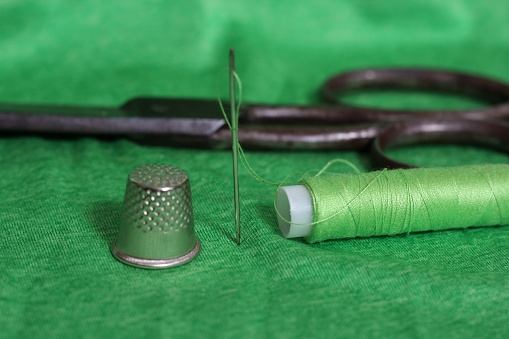 A spool of thread, thimble, needle and vintage scissors on green fabric