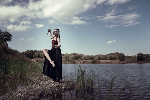A Caucasian woman holding knife and standing near lake