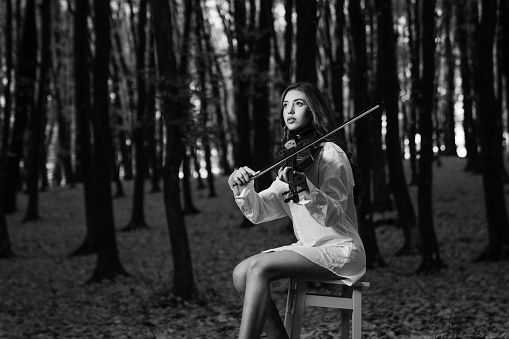 A Caucasian woman playing violin in forest