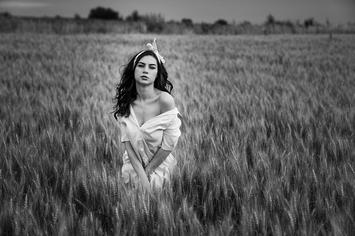 A Caucasian woman wearing white drees and standing in wheat field