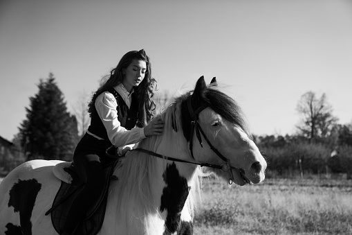 A grayscale shot of a young female riding a horse