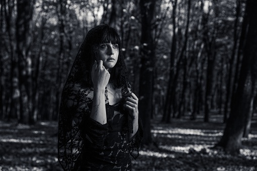 A grayscale of a young mourning woman with bangs in a black dress in a field