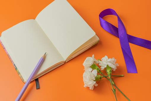 notepad and pencil with purple ribbon anf flowers  on a cheerful orange background