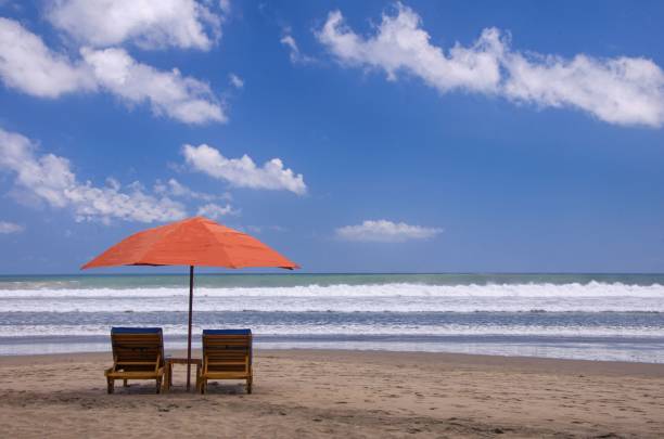 istock Two chairs under an orange umbrella on the beach with a cloudy blue sky in the background 1459564306