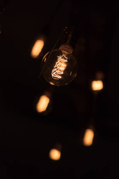 istock Lit spiral in a light bulb in a dark room with lit blurred bulbs on the background 1459565078