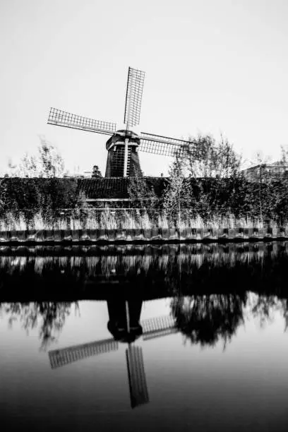 Photo of Vertical grayscale shot of a traditional windmill with reflection in the water in Amsterdam, Holland