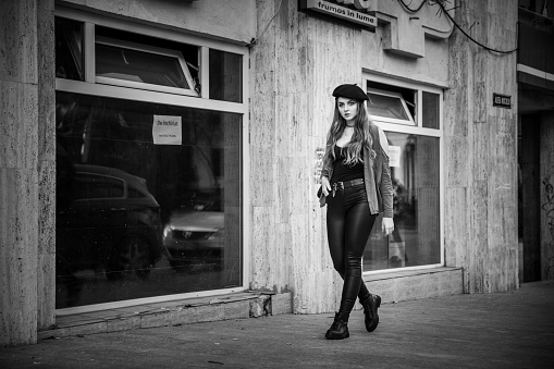 A grayscale shot of a Caucasian woman wearing a casual outfit and a beret posing outdoors