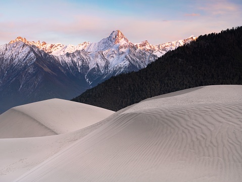 Scenic view of sand dunes with snow capped mountains in background at sunset in Yarlung Tsangpo Grand Canyon, West China