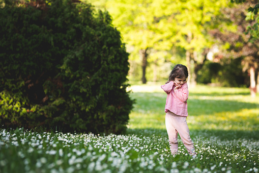 Playful little girl having fun in the park with blooming meadow in spring. 3 years old cute toddle