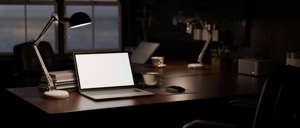 istock Modern dark office at night with laptop mockup, light from table lamp, and office accessories 1459571019