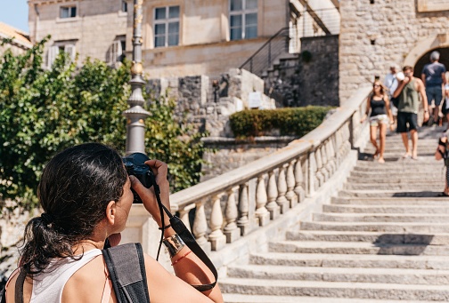 A young woman using a digital camera, taking photos of old town of Korcula in Croatia