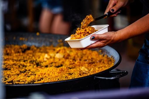 A chief is cooking paella outdoors in a big frying pan
