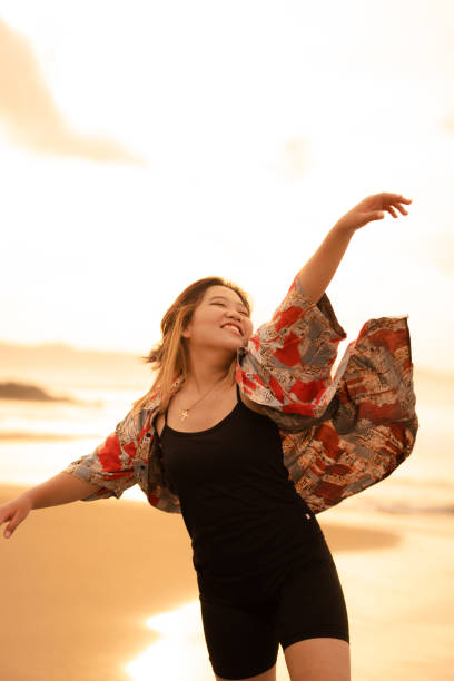 una mujer asiática con cabello rubio y una camisa roja camina por la playa para disfrutar de la vista al mar - stone wellbeing zen like blue fotografías e imágenes de stock