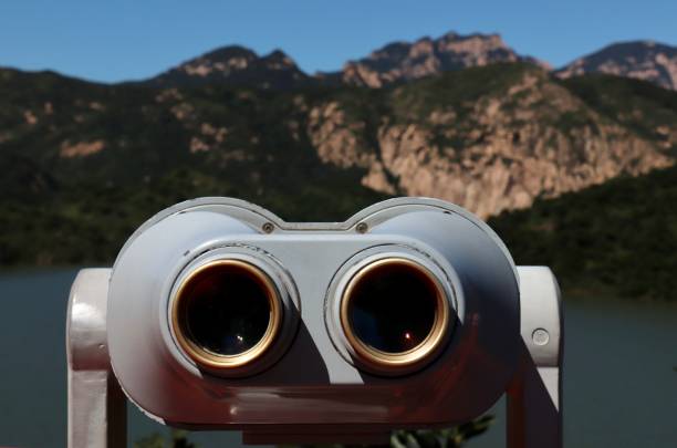 istock Binoculars with a river and rocky mountains covered with green trees in the background 1459574424