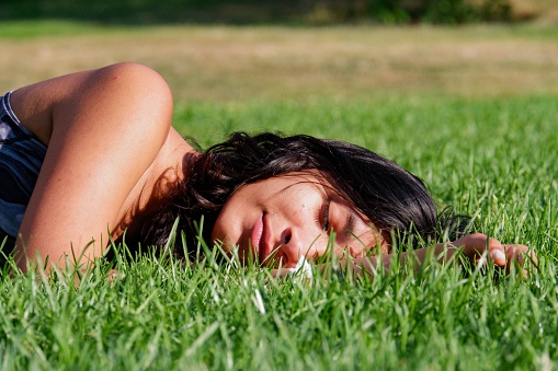 A beautiful closeup of a female lying on green grass ground covered with sun rays