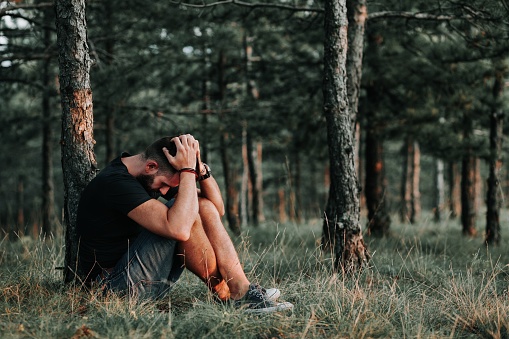 A young depressed male sitting alone in the woods