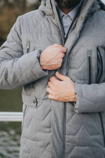 vertical shot of a man zippering his puffy gray overcoat - zippering imagens e fotografias de stock