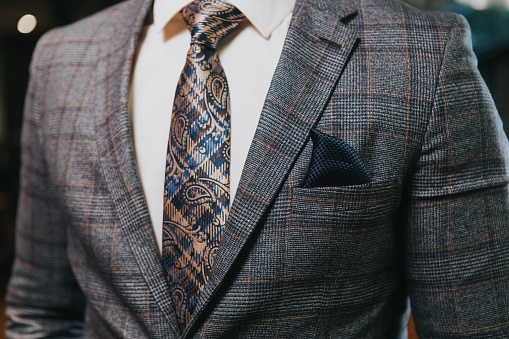 A closeup of the torso of a man in a gray check suit and white shirt with check paisley tie