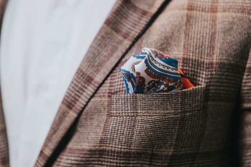 A closeup of a man's brown check suit jacket with a paisley pocket square