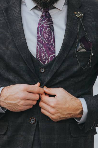 istock A man buttoning his gray check jacket partnered with purple paisley tie and a lapel chain 1459576586