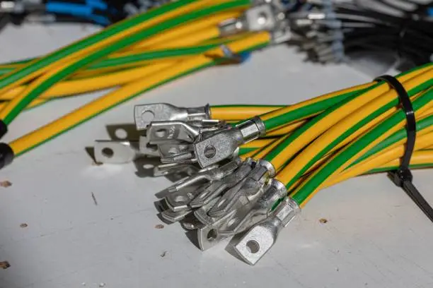 Photo of Closeup of green-yellow electrical wires with lugs under the sunlight.