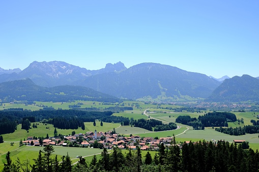 An aerial shot of the small village in the green field with mountains in the backgrouund