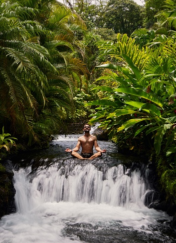 Cheerful man meditating sitting in streaming water of Tabacon waterfall, Costa Rica