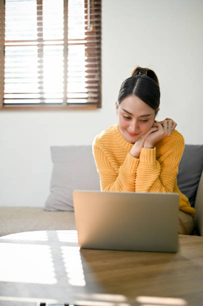istock Charming Asian woman working from home, using her laptop while sitting on sofa. 1459580026