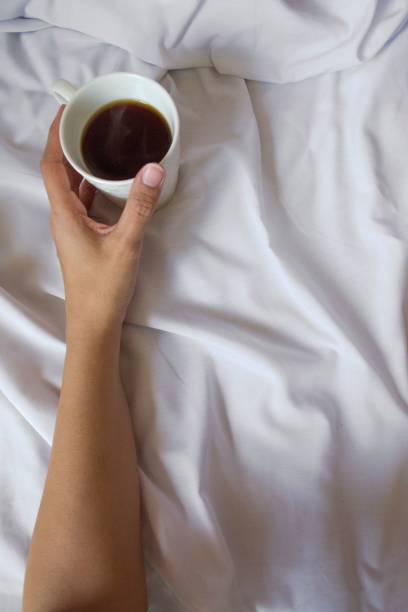 istock Top view of a hand holding a drink in ceramic cup on white cloth surface 1459580310