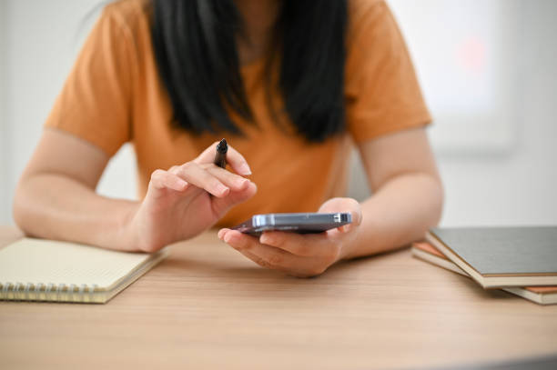 istock Young Asian woman holding pen and using her smartphone at her table. 1459582242