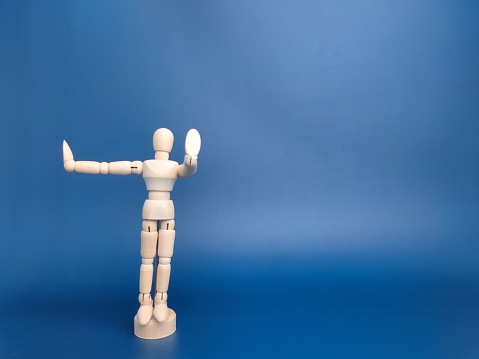 Wooden mannequin posed with one hand in front and the other one on the side on a blue background