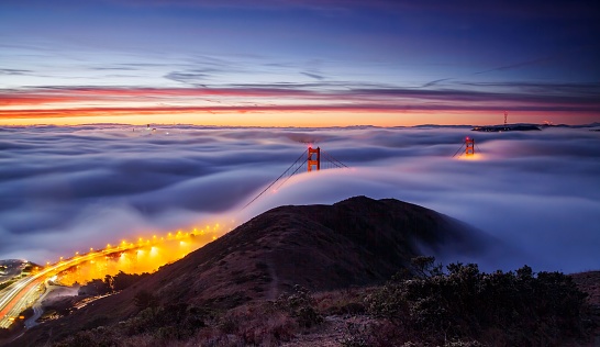 The aerial long exposure view of the clouds covering the Golden gates bridge in the evening