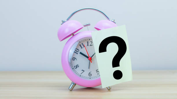 istock Pink alarm clock with a yellow post-it note attached to the clock lies on the table with a QuestionMark symbol. Horizontal composition with copy space. 1459583702