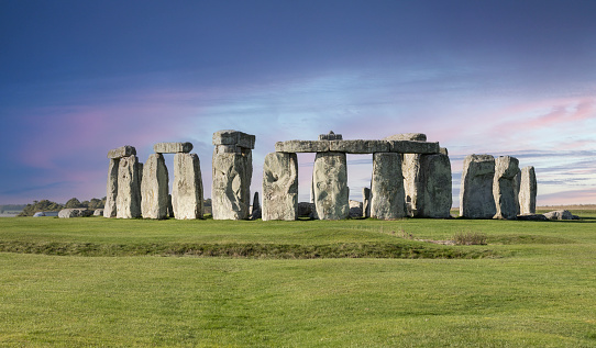 A Pink Super Full moon rises  over the ancient stone circle of Stonehenge in Wiltshire, UK as sheep graze in adjacent fields.\nStraight shot of a natural event, no photo manipulation