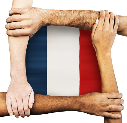 Multiracial group of hands and arms of men and women clasping each other, signifying unity, solidarity, cooperation and teamwork, around the flag of France.