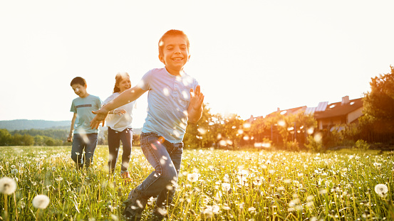 Smiling children playing in meadow against sky during sunset.