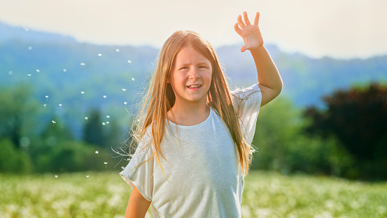 Portrait of smiling girl playing with dandelion seeds in meadow during sunny day.