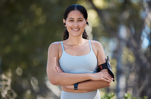Portrait, exercise and woman, arms crossed and motivation in park with music, fitness and arm band. Happy young athlete, healthy lifestyle or outdoor training, runner and wellness, energy and workout